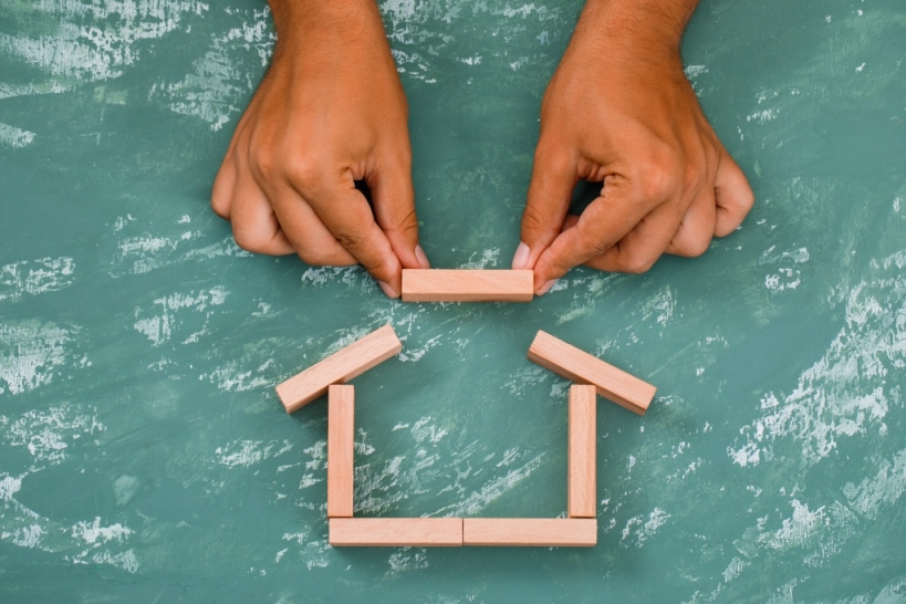 Business and real estate concept on plaster background flat lay. hand building house with wooden blocks.